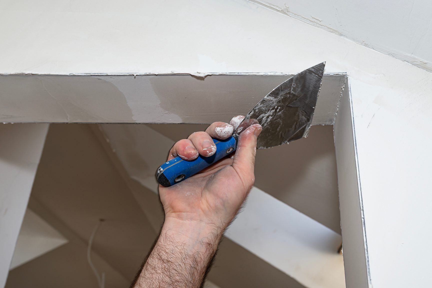 A close view of a gloved hand pressing a taping knife against a freshly finished drywall corner.